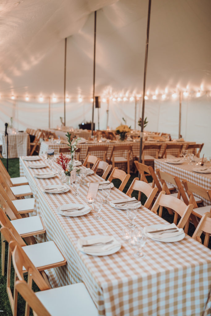 rustic tented welcome dinner with taupe & white checkered table cloths, wood folding garden chairs, and bud vase centerpieces