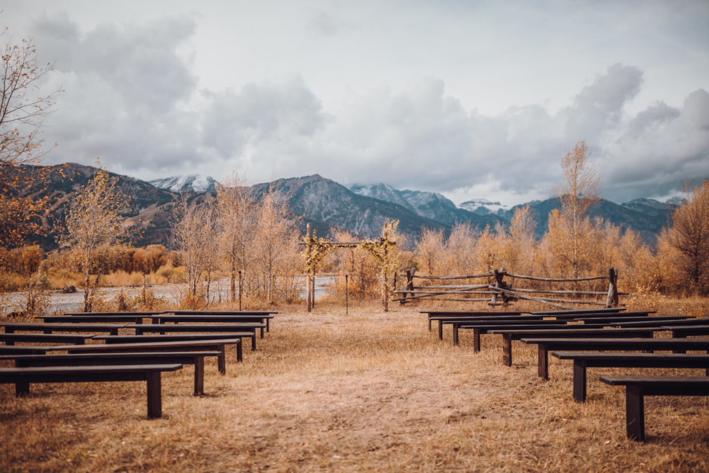 riverside ceremony in Jackson Hole at the base on the Tetons with benches for ceremony seating and natural birch wood arbor decorated with seasonal branches