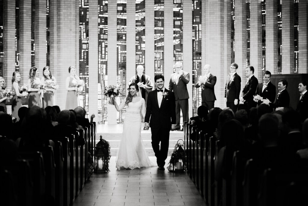 A bride and groom wave to their guests as they recess back up the aisle after their church wedding ceremony. 