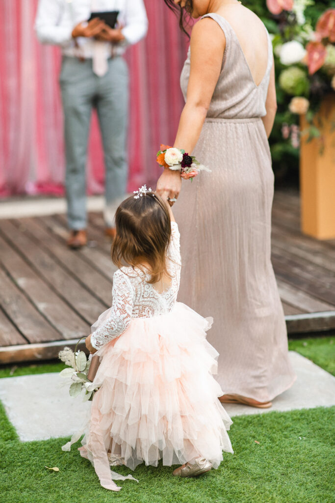 A flower girl is lead to the altar by her mom, a bridesmaid, during this outdoor garden wedding ceremony.
