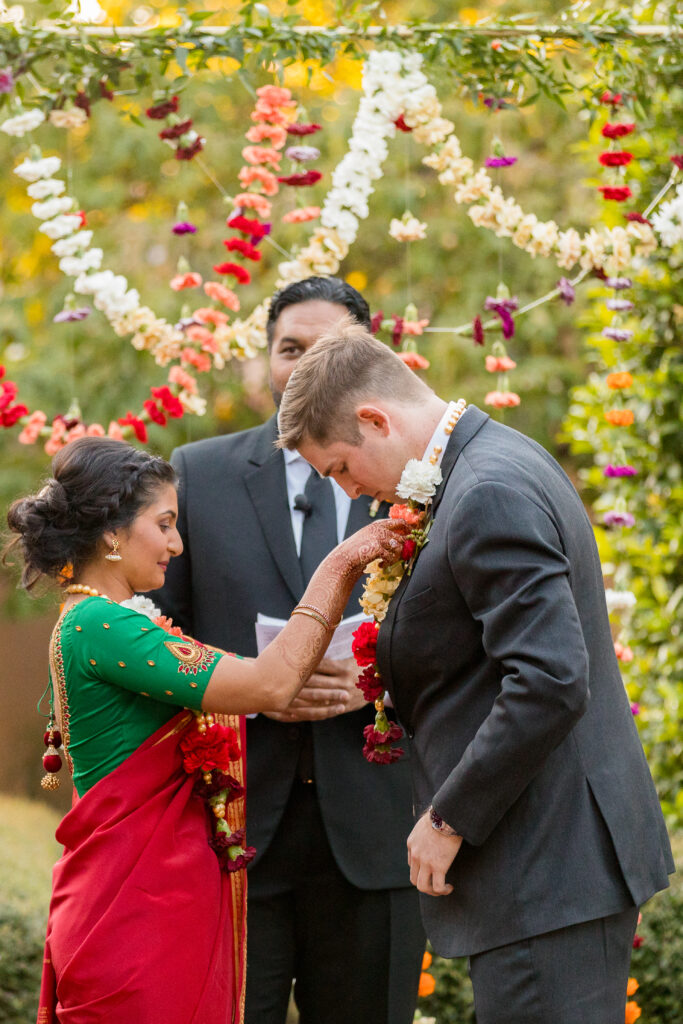 A bride places the garland around her groom's neck during their multicultural wedding ceremony.