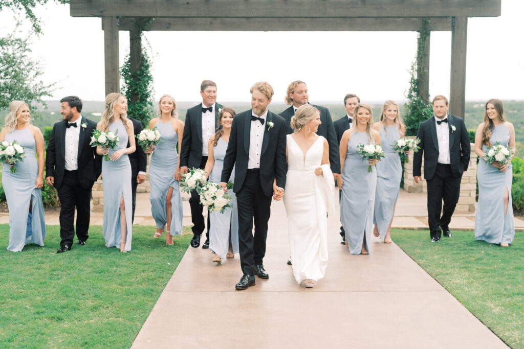 A couple walk leisurely with their wedding party on the grounds of Canyon Ridge in Dripping Springs, Texas.